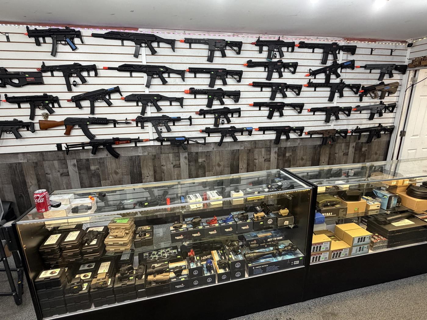 Wall of airsoft rifles above glass display cases